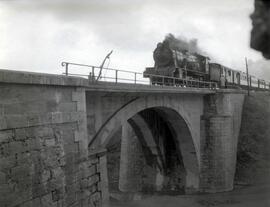 Composición de viajeros remolcada por locomotora a vapor atravesando el puente de hormigón Henare...