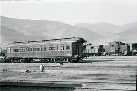 Coche de viajeros tipo costa con linternón en la estación de Portbou, tras él una locomotora de m...